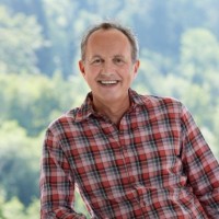 Smiling man in plaid shirt with forest background.